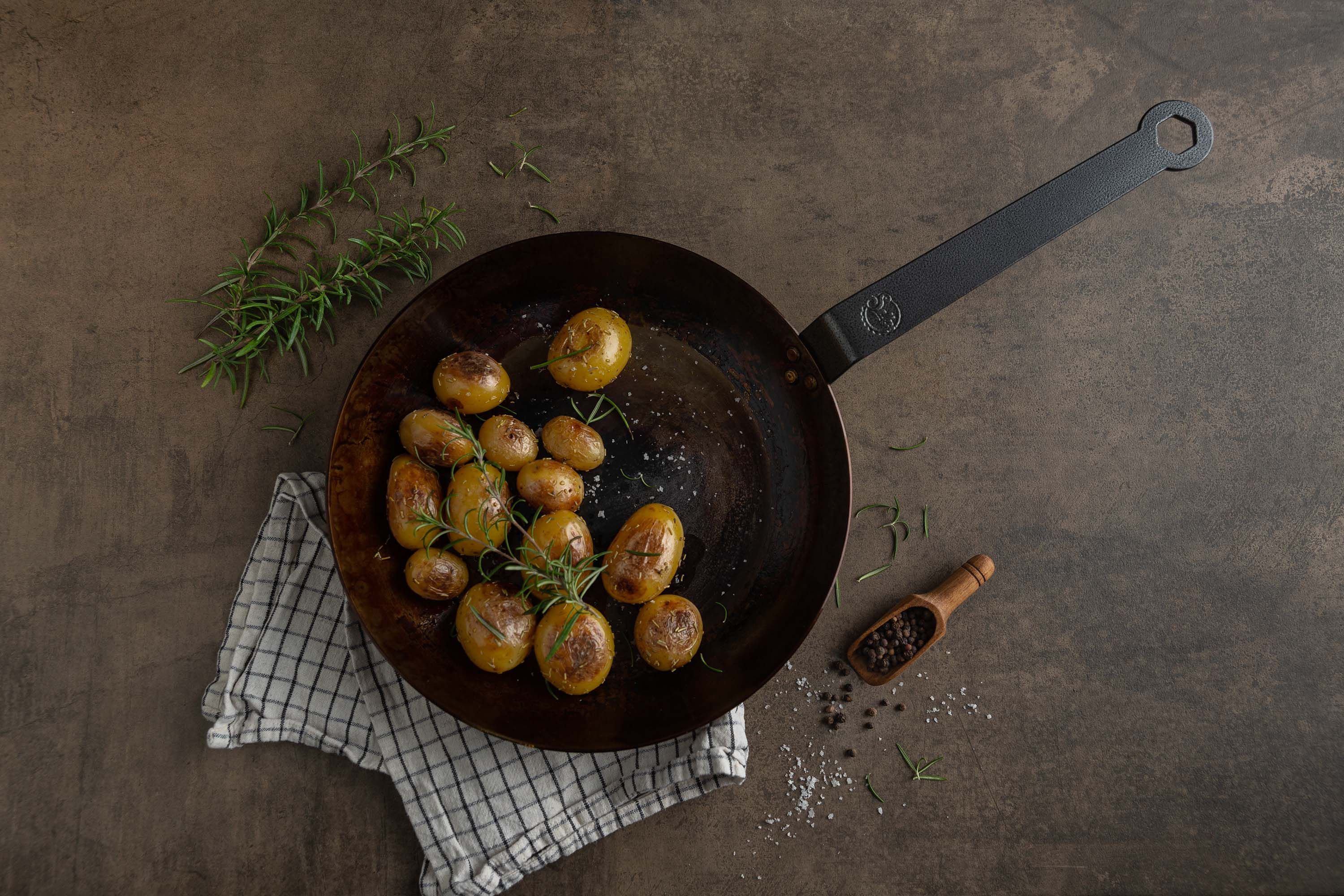 Eine Eisenpfanne steht mit Kartoffeln darin auf einem Tisch